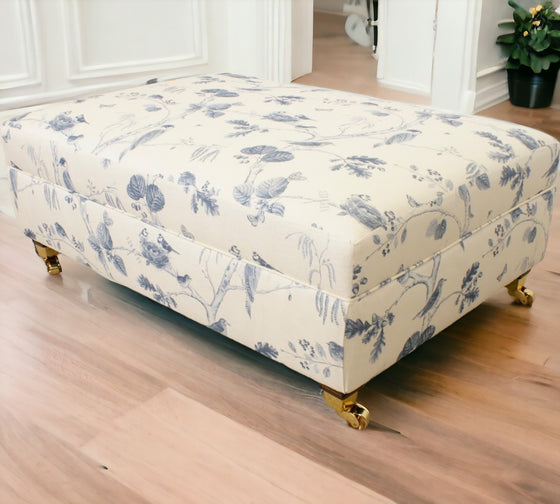 Large oblong footstool set at a angle with sanderson woodland chorus fabric that has woodland scenery with birds in blue and cream with brass castor foot