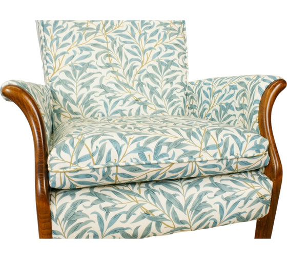 Parker Knoll Froxfield small chair with antique wooden front arms that swoop outwards and upholstered in teal coloured leafy fabric with a white backing.
