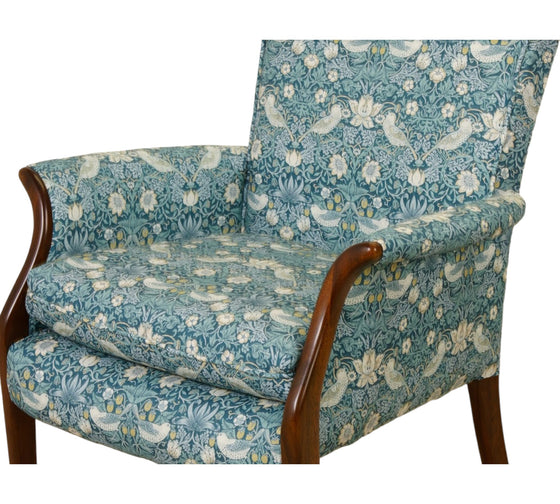 small chair with dark wood fronted arms upholstered in a repetitive busy fabric with birds and strawberries in a Teal colour 