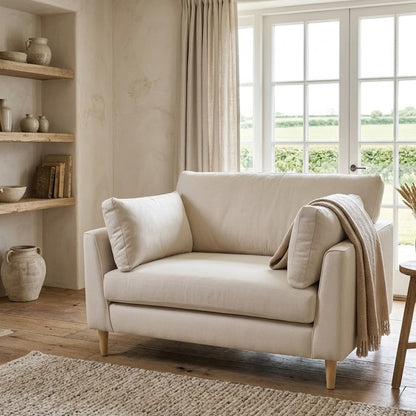 Beige sofa in a living room with large windows and wooden furniture.