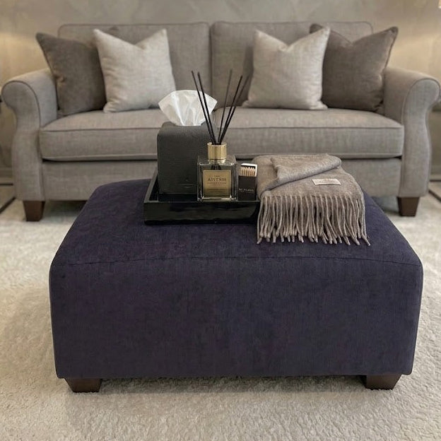 Gray sofa with decorative pillows and a purple ottoman in a living room setting.