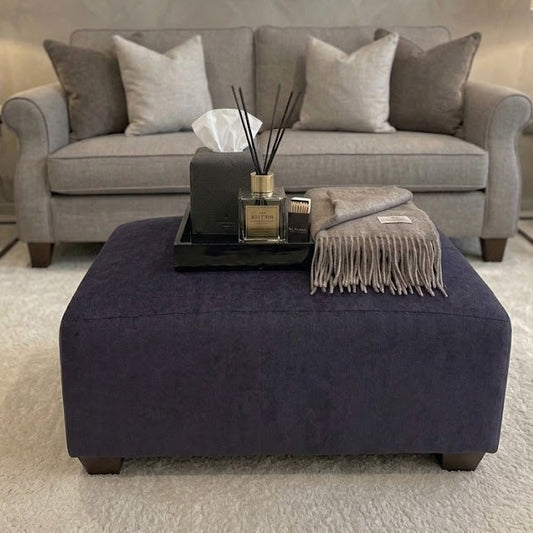 Gray sofa with decorative pillows and a purple ottoman in a living room setting.