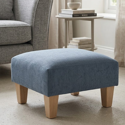 Blue ottoman in a living room setting with a gray armchair and light curtains.