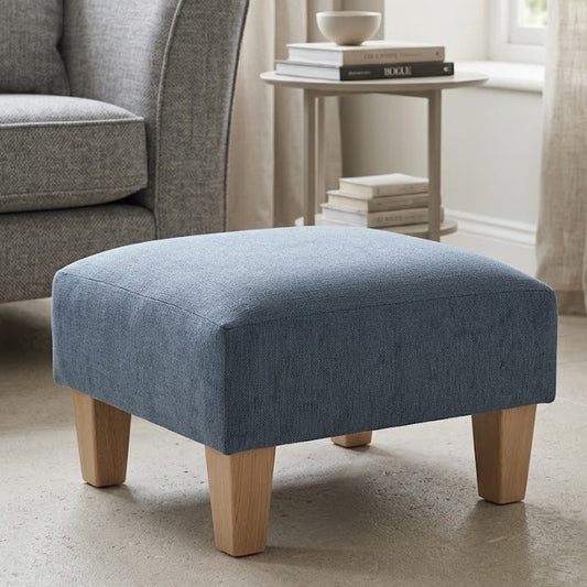 Blue ottoman in a living room setting with a gray armchair and light curtains.