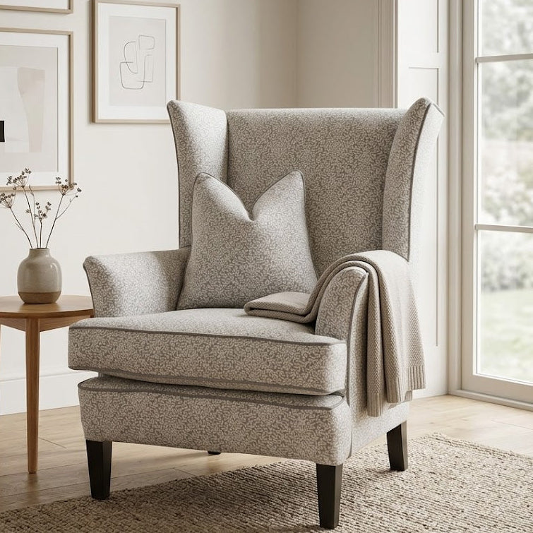 Gray armchair in a room with framed pictures on the wall and a small table with a vase.