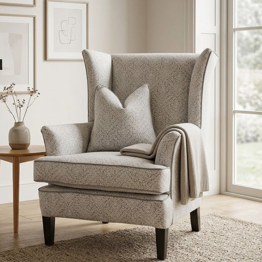 Gray armchair in a room with framed pictures on the wall and a small table with a vase.