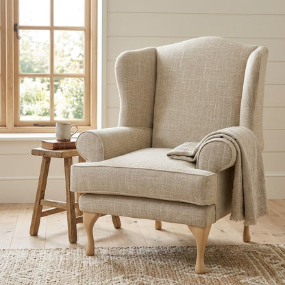 Beige armchair with a blanket in a cozy room with a window and wooden stool.