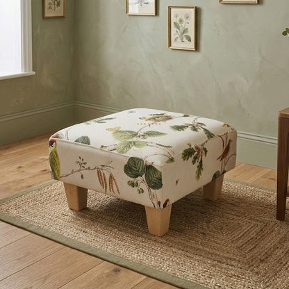 Floral-patterned ottoman in a room with a window, rug, and side table.
