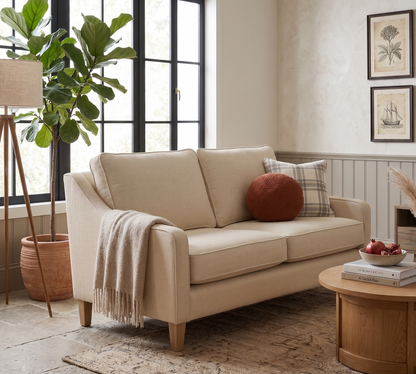 Beige sofa in a living room with a round wooden coffee table, plant, and framed pictures on the wall.