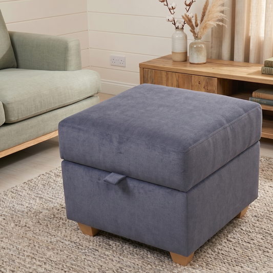 Blue ottoman in a living room setting with a sofa and wooden cabinet in the background.