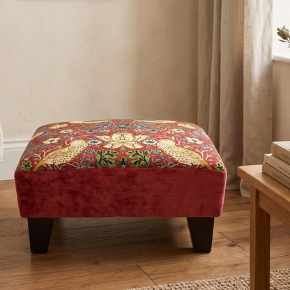 Decorative red ottoman with floral pattern in a living room setting.