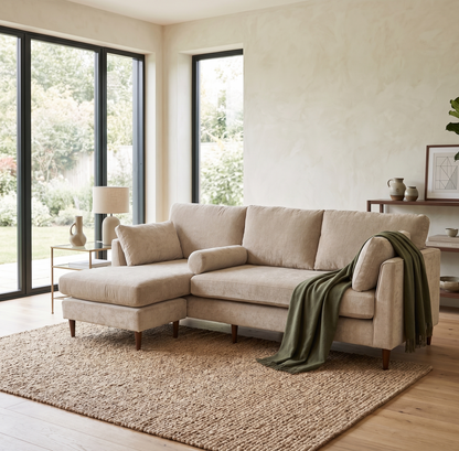 Beige sectional sofa in a living room with large windows and a rug.