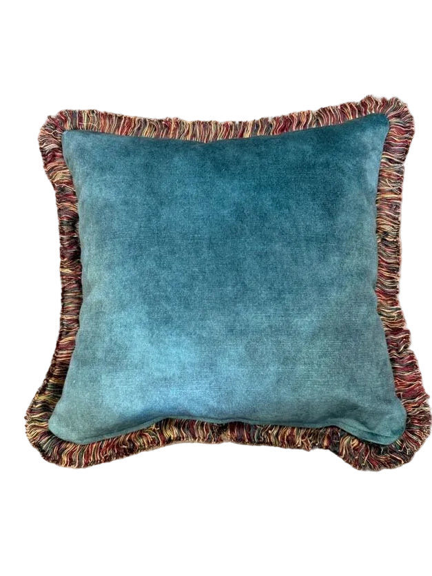 A square green velvet throw pillow with a multicolor fringed border, photographed from directly above on a beige carpet background.