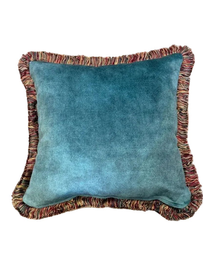 A square green velvet throw pillow with a multicolor fringed border, photographed from directly above on a beige carpet background.