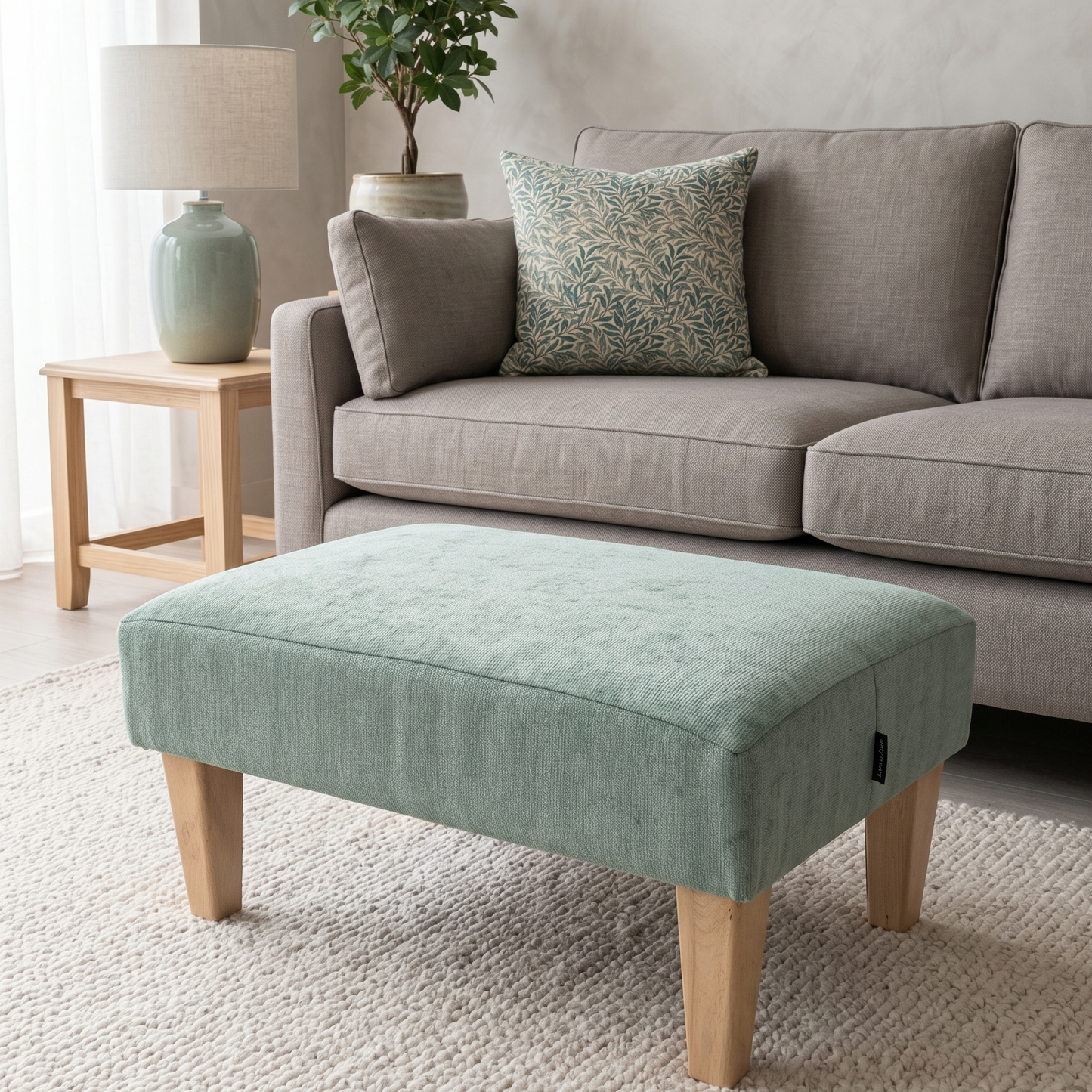 Light green ottoman in front of a gray sofa with decorative pillows in a living room setting.