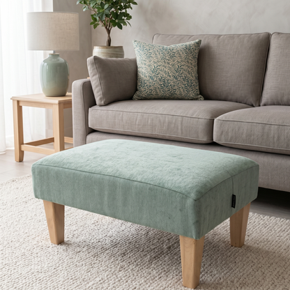 Light green ottoman in front of a gray sofa with decorative pillows in a living room setting.