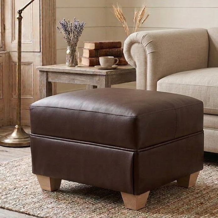 Brown leather ottoman in a living room setting with a beige sofa and wooden floor.