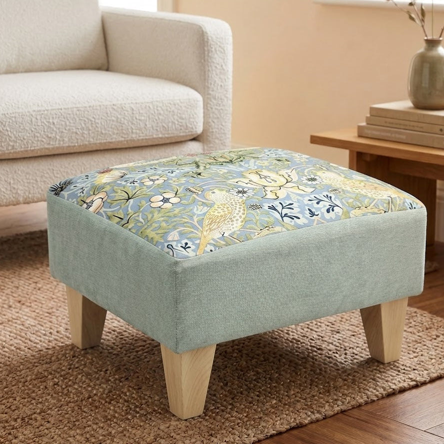 Fabric ottoman with floral pattern on a wooden floor in a living room setting.