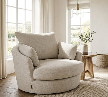 Beige armchair in a bright living room with large windows and wooden furniture.