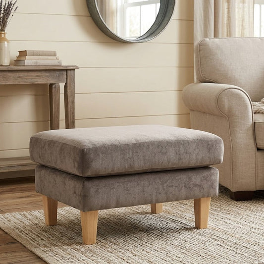 Gray ottoman in a living room setting with a beige armchair and wooden table.