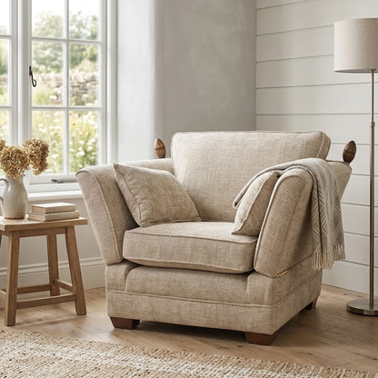 Beige armchair in a room with a window, lamp, and small table.